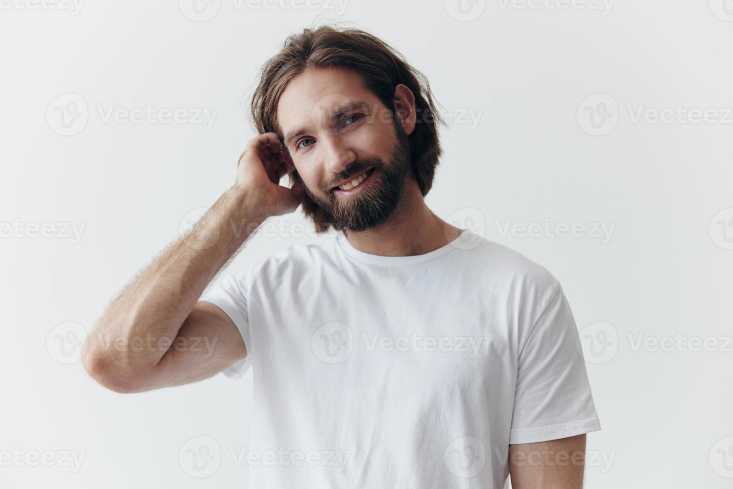 portrait de une de bonne humeur homme avec une noir épais barbe et longue cheveux avec une gentil sourire dans une blanc T-shirt sur une blanc isolé Contexte photo