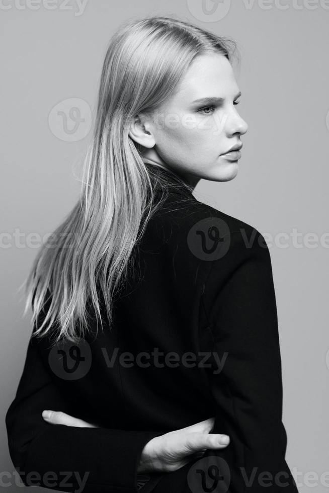 le concept de art la photographie. une élégant fille des croix sa bras derrière sa retour se tourne sa tête et pose avec sa retour dans une noir veste dans le studio. mode bannière photo