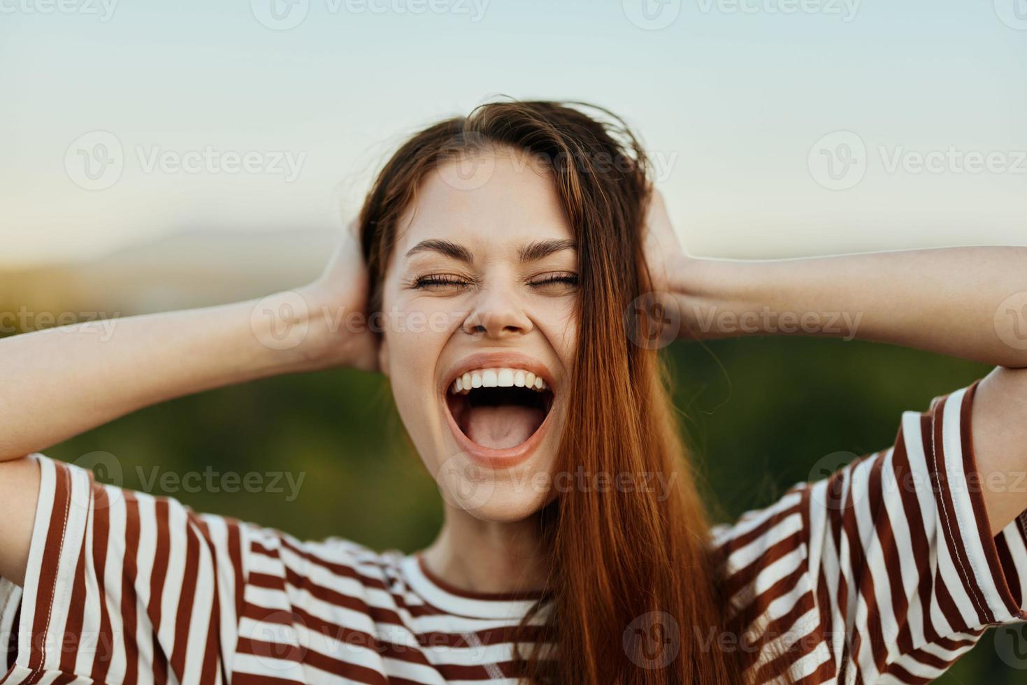 une Jeune femme dans une rayé T-shirt Cordialement des rires avec sa bouche ouvert tandis que en voyageant contre le toile de fond de l'automne la nature photo