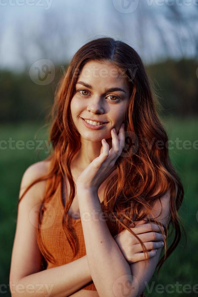 portrait de une femme avec une magnifique sourire dans été vert la nature contre le herbe, à la recherche en dehors à le réglage Soleil. le concept de santé et beauté photo