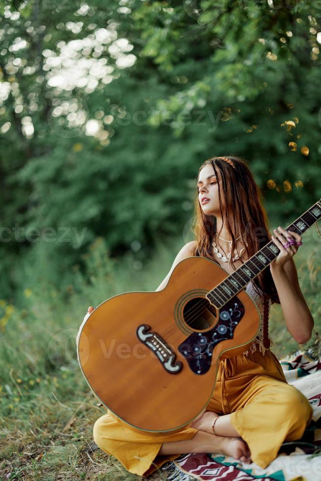 une fille dans éco-vêtements hippie séance avec une guitare et à la recherche à une le coucher du soleil dans le été photo