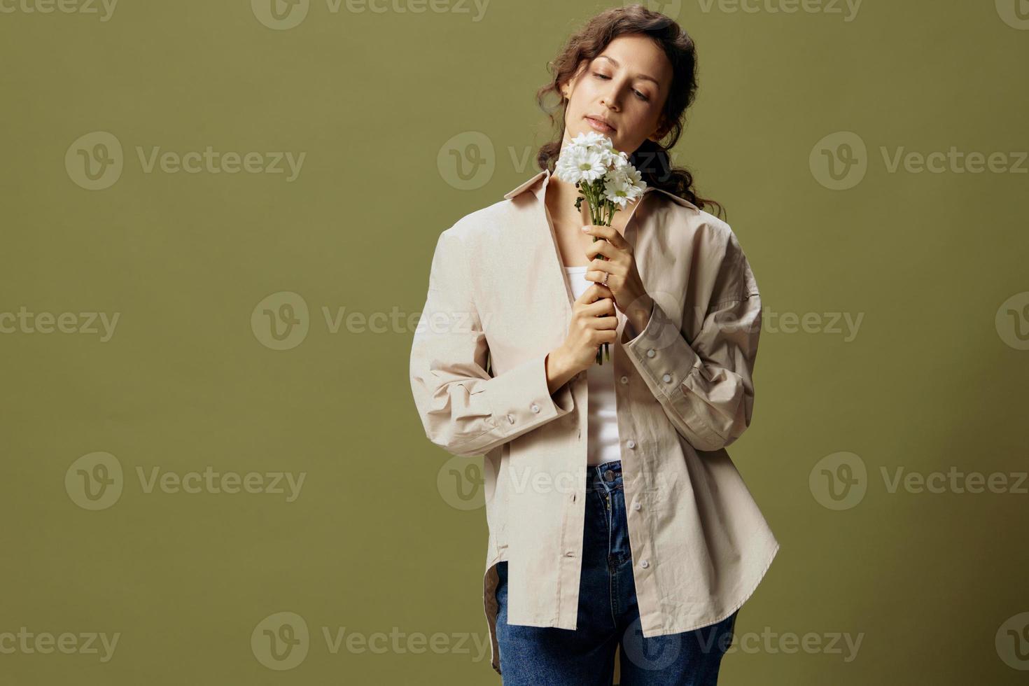 calme mignonne de bonne humeur frisé magnifique femelle dans lin décontractée chemise tenir camomille regards avec l'amour à fleurs posant isolé sur plus de olive vert pastel Contexte. la nature est beauté concept. copie espace photo