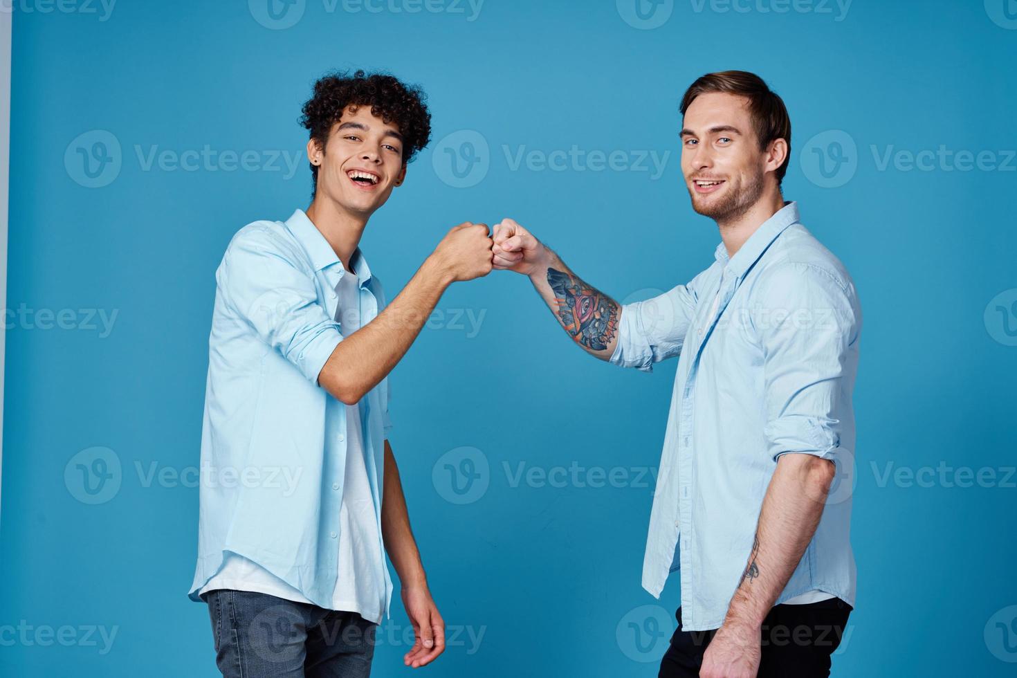 aux cheveux bouclés gars dans une chemise salue le sien ami sur une bleu Contexte photo