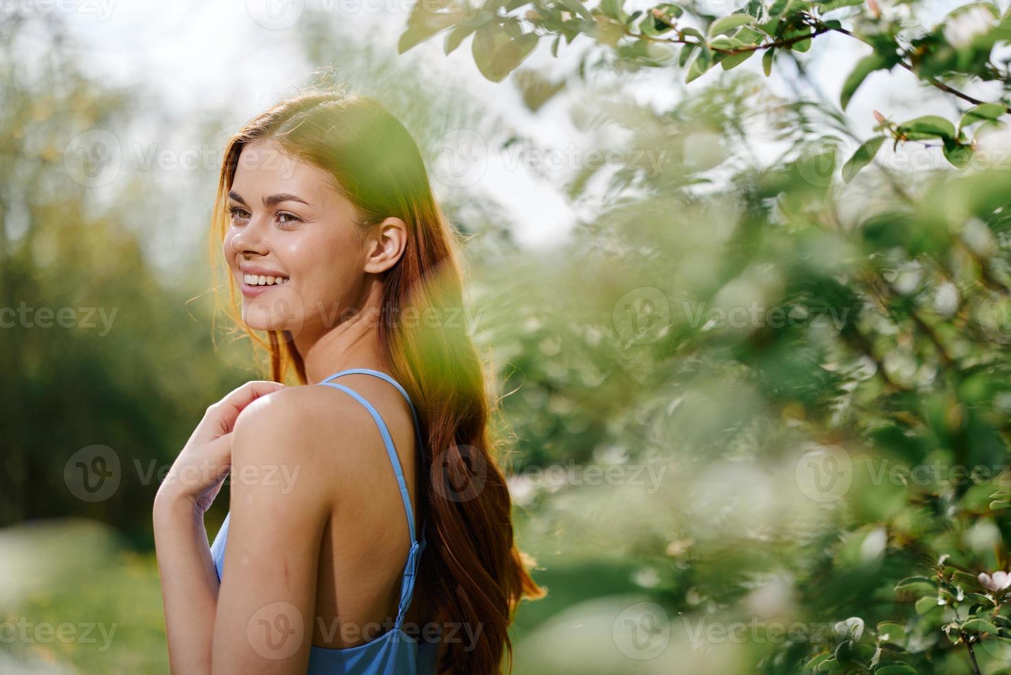 femme sourire avec les dents dans profil bonheur dans la nature dans le été près une vert arbre dans le jardin de le parc dans une bleu robe, le concept de aux femmes santé et beauté avec la nature le coucher du soleil photo