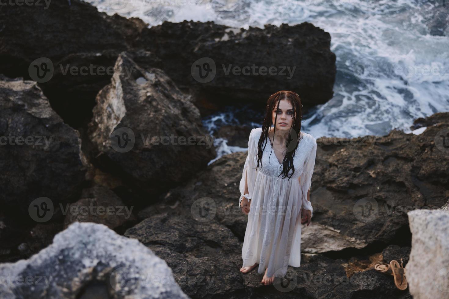 femme avec humide cheveux dans une blanc robe des stands sur le des pierres Haut vue photo