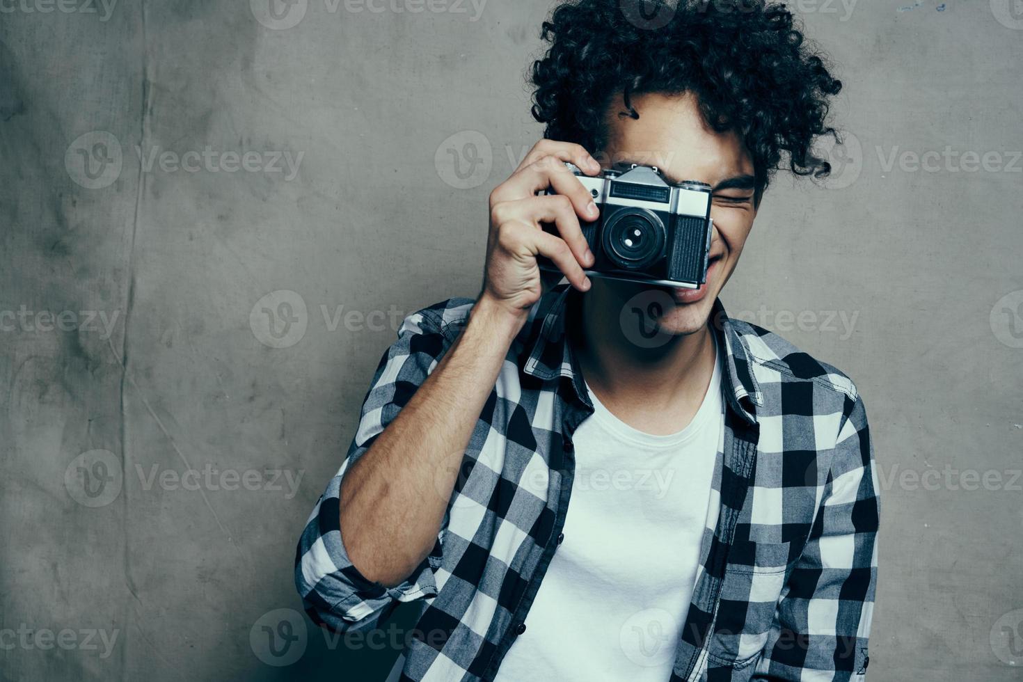 gars avec une caméra dans le sien mains sur une gris Contexte à l'intérieur loisir plaid chemise modèle photo