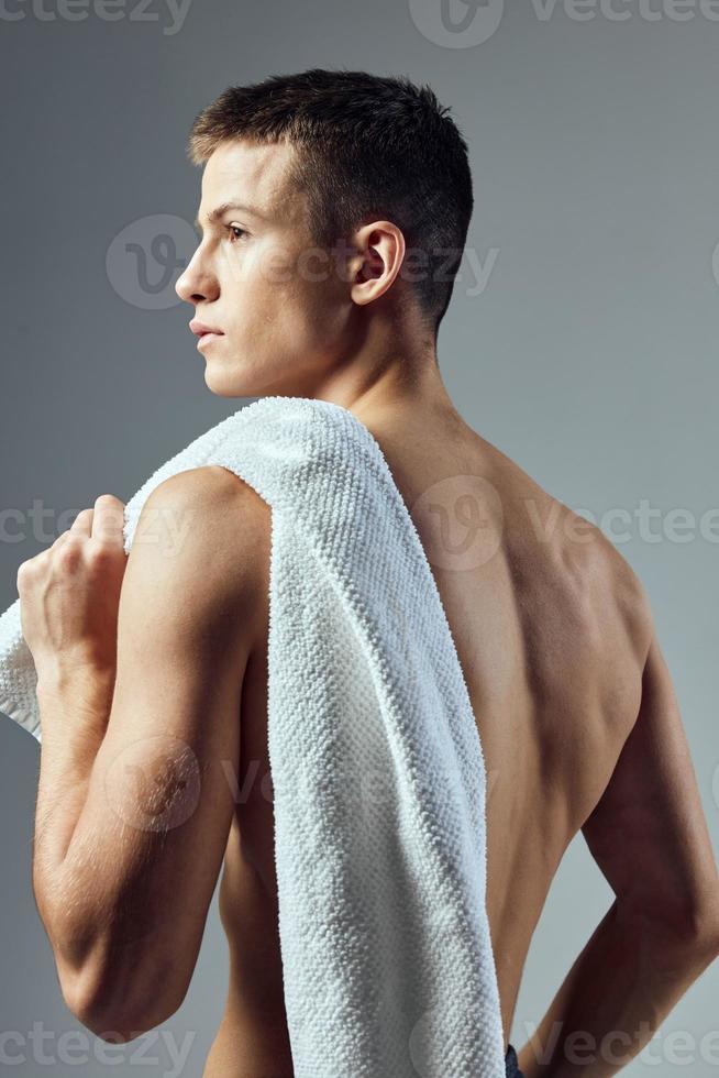 Beau Jeune Homme Debout Dans La Salle De Bain Avec Une Serviette Blanche  Sur Les Épaules. Brunette Mec Musclé Avec Un Torse Torse Nu Tenant Une  Serviette Et Skincare Son Visage, Vérifiant