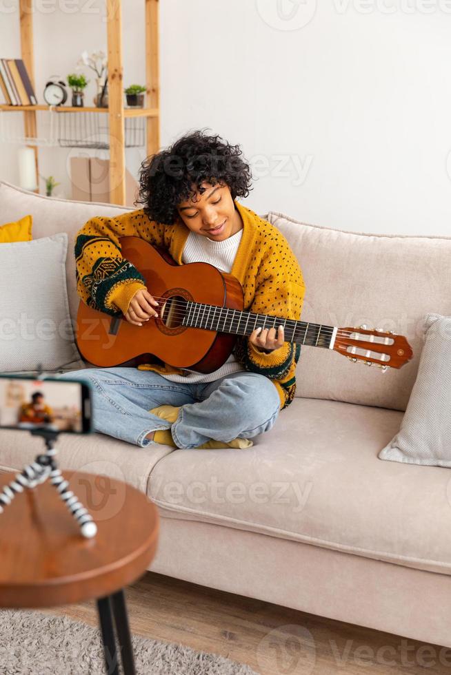 blogueur guitariste. content africain américain fille blogueur en jouant guitare en chantant chanson enregistrement vlog. social médias influenceur femme diffusion enregistrement à Accueil studio. la musique contenu créateur diffuser. photo