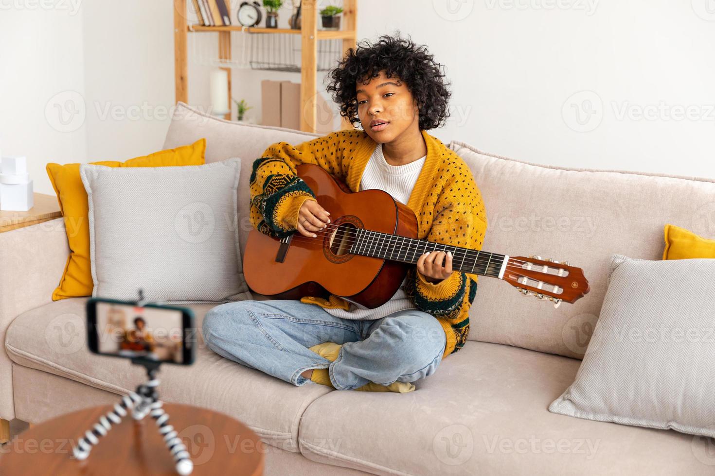 blogueur guitariste. africain américain fille blogueur en jouant guitare parlant à webcam enregistrement vlog. social médias influenceur femme diffusion à Accueil à l'intérieur. la musique contenu créateur diffuser Didacticiel. photo