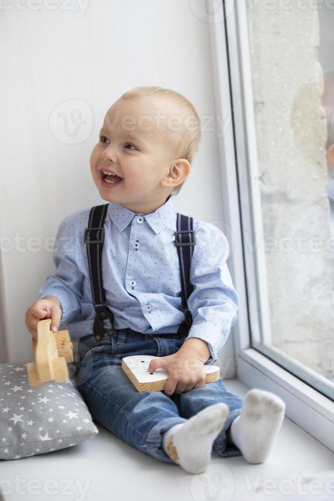 peu bébé près le la fenêtre. le de bonne humeur enfant avec une jouet est assis sur une fenêtre seuil. photo