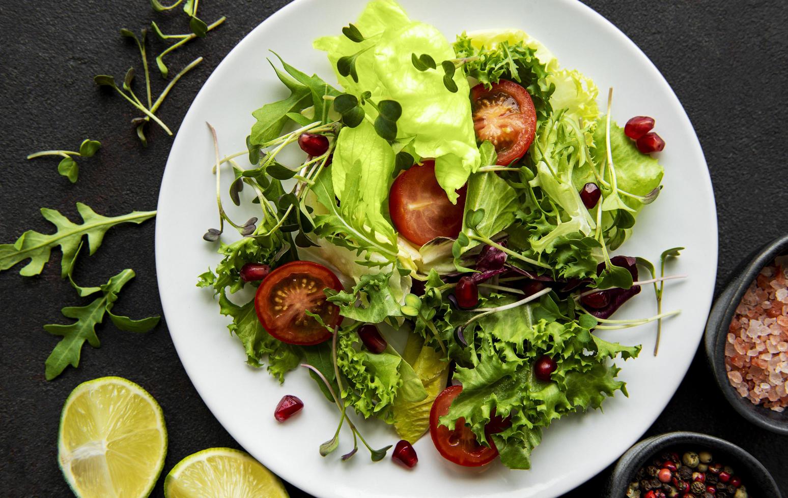 Salade mixte verte fraîche avec des tomates et des microgreens sur fond de béton noir photo