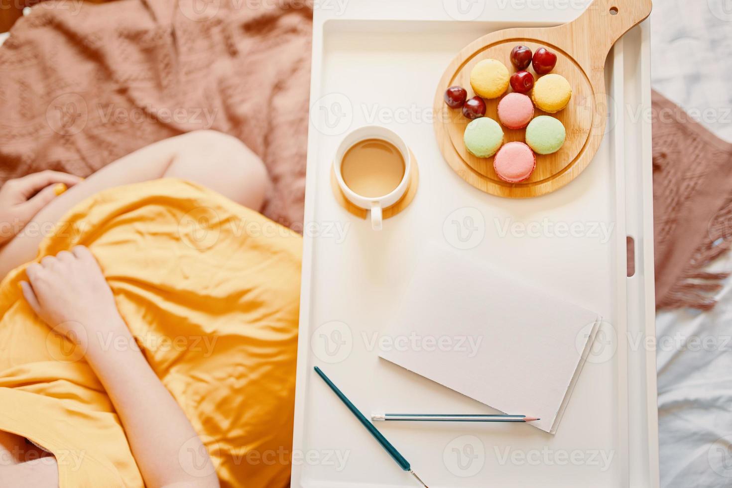 fille en robe jaune assis sur le lit avec plateau de café, dessert et cahier vide photo