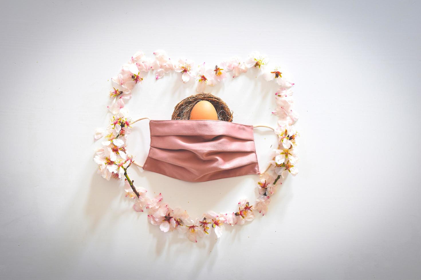 Fleurs de marguerite de printemps sous la forme d'un coeur avec masque rose couvrant un oeuf de Pâques photo