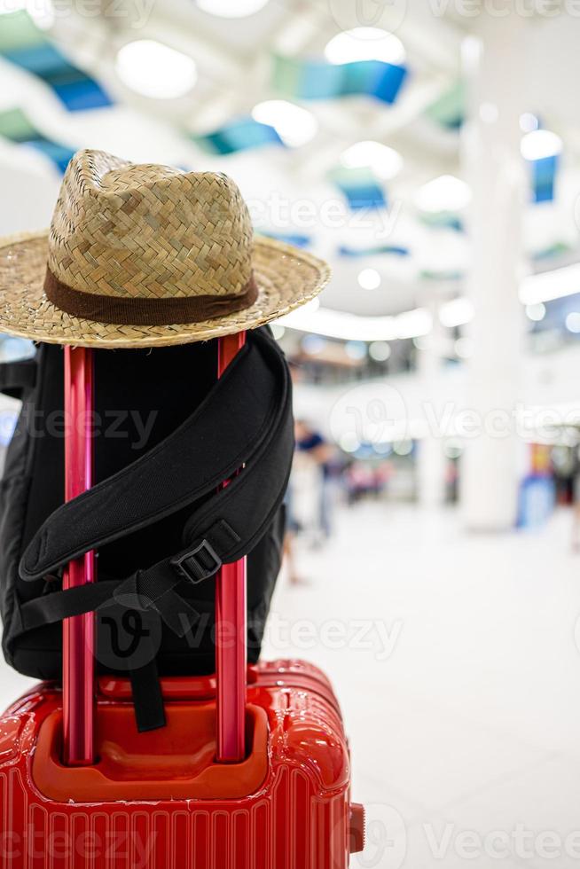 Chapeau de paille accroché sur la poignée de bagage rouge avec fond de voyage flou photo
