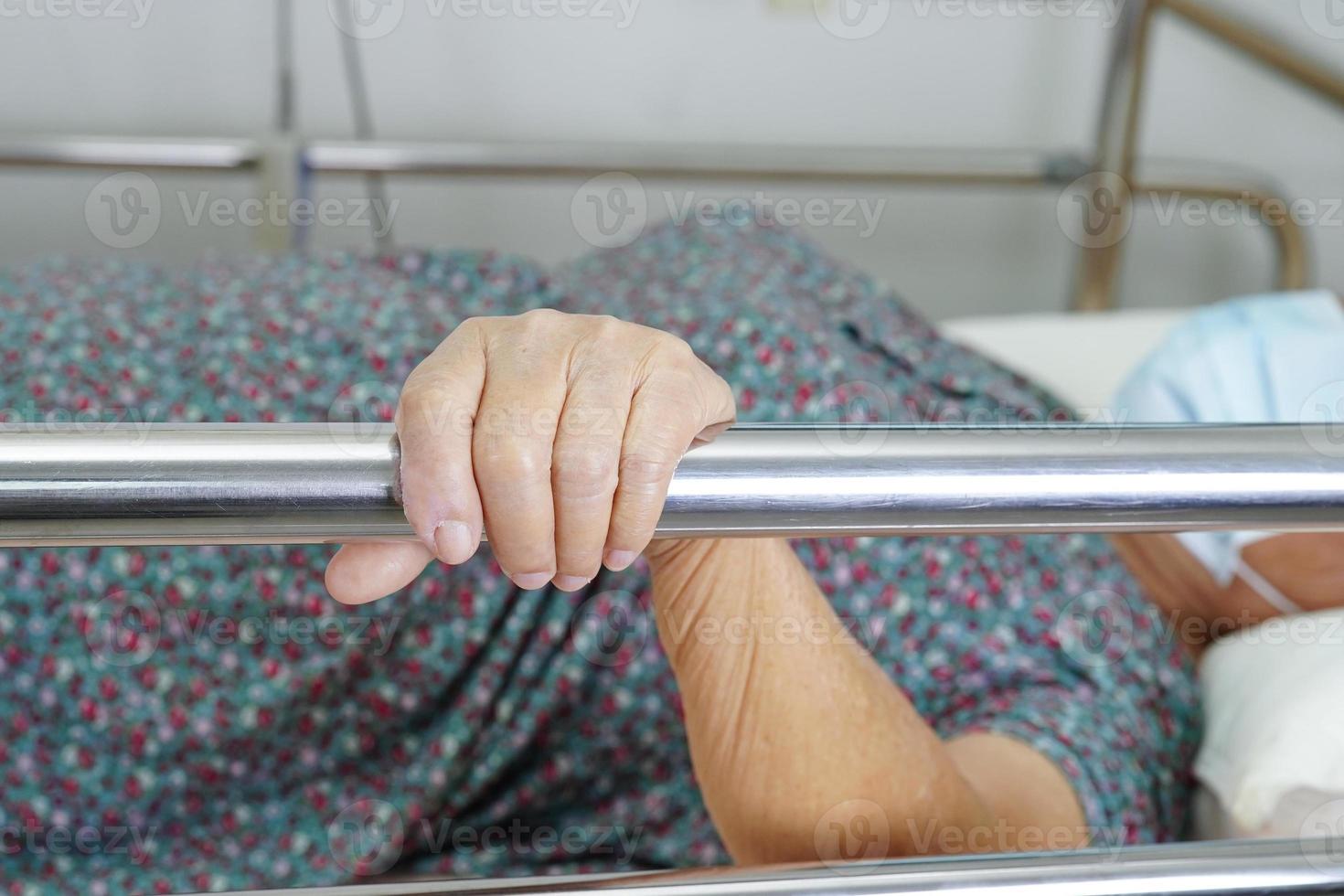 une femme âgée asiatique âgée patiente tenant une barrière de lit tout en se couchant avec espoir en attendant sa famille à l'hôpital. photo