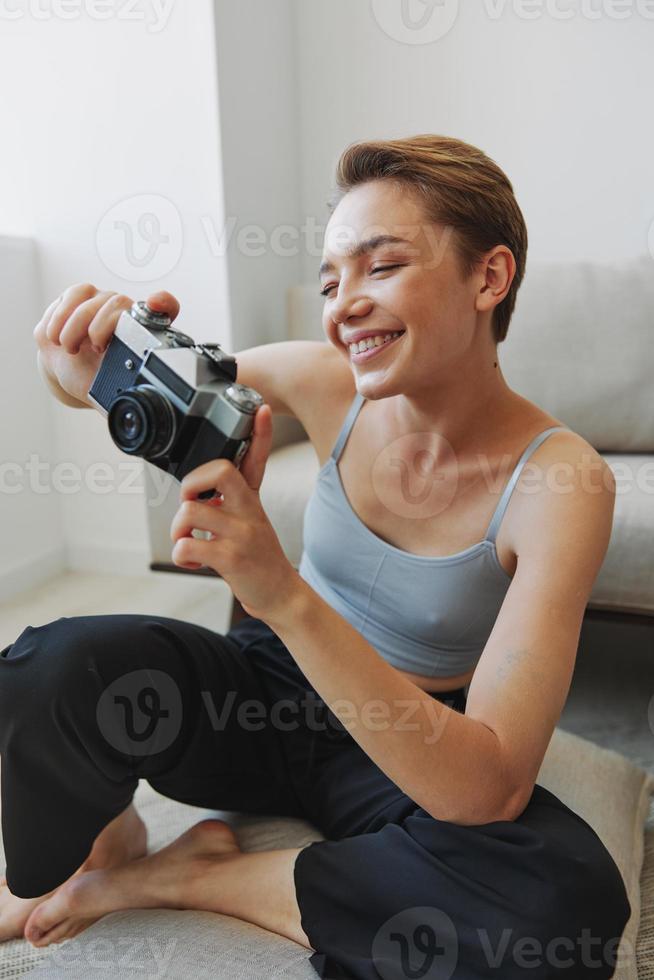 content sourire femme en portant un vieux caméra et prise des photos de se comme une fin de semaine photographe dans Accueil vêtements avec une court la Coupe de cheveux cheveux sans pour autant filtres sur une blanc arrière-plan, gratuit copie espace