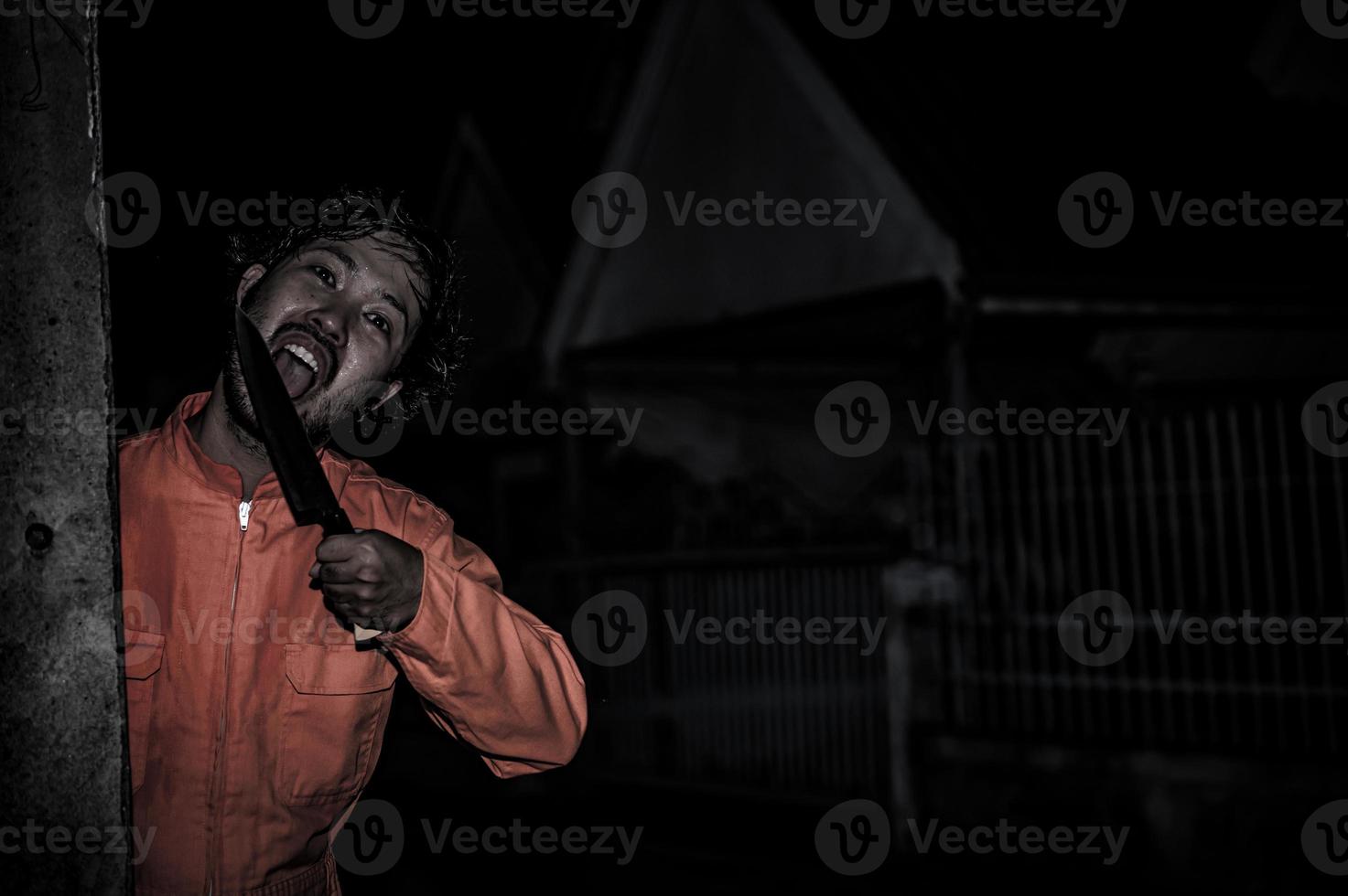 asiatique Beau homme porter pitre masque avec arme à le nuit scène, halloween Festival concept, horreur effrayant photo de une tueur dans Orange tissu