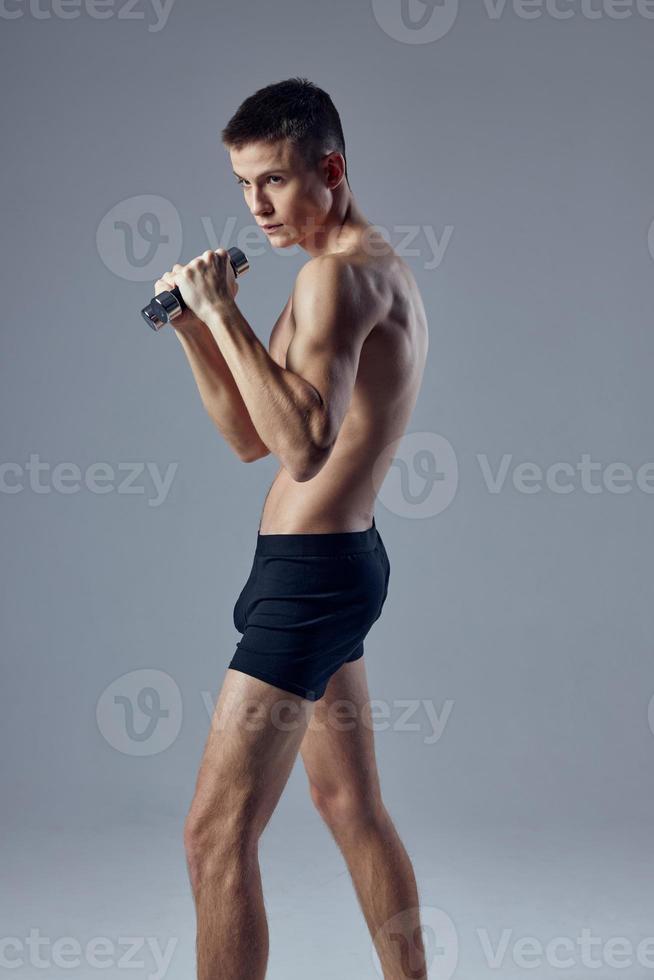 sportif homme posant dans noir short avec haltères dans mains faire des exercices aptitude isolé Contexte photo