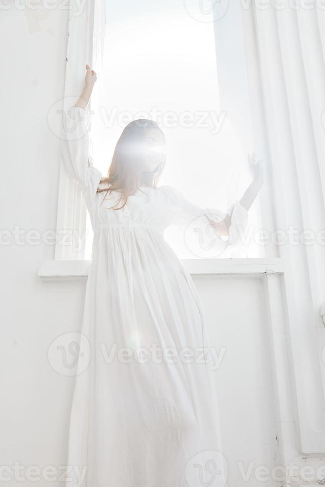femme dans blanc robe près fenêtre posant romance de le Soleil photo