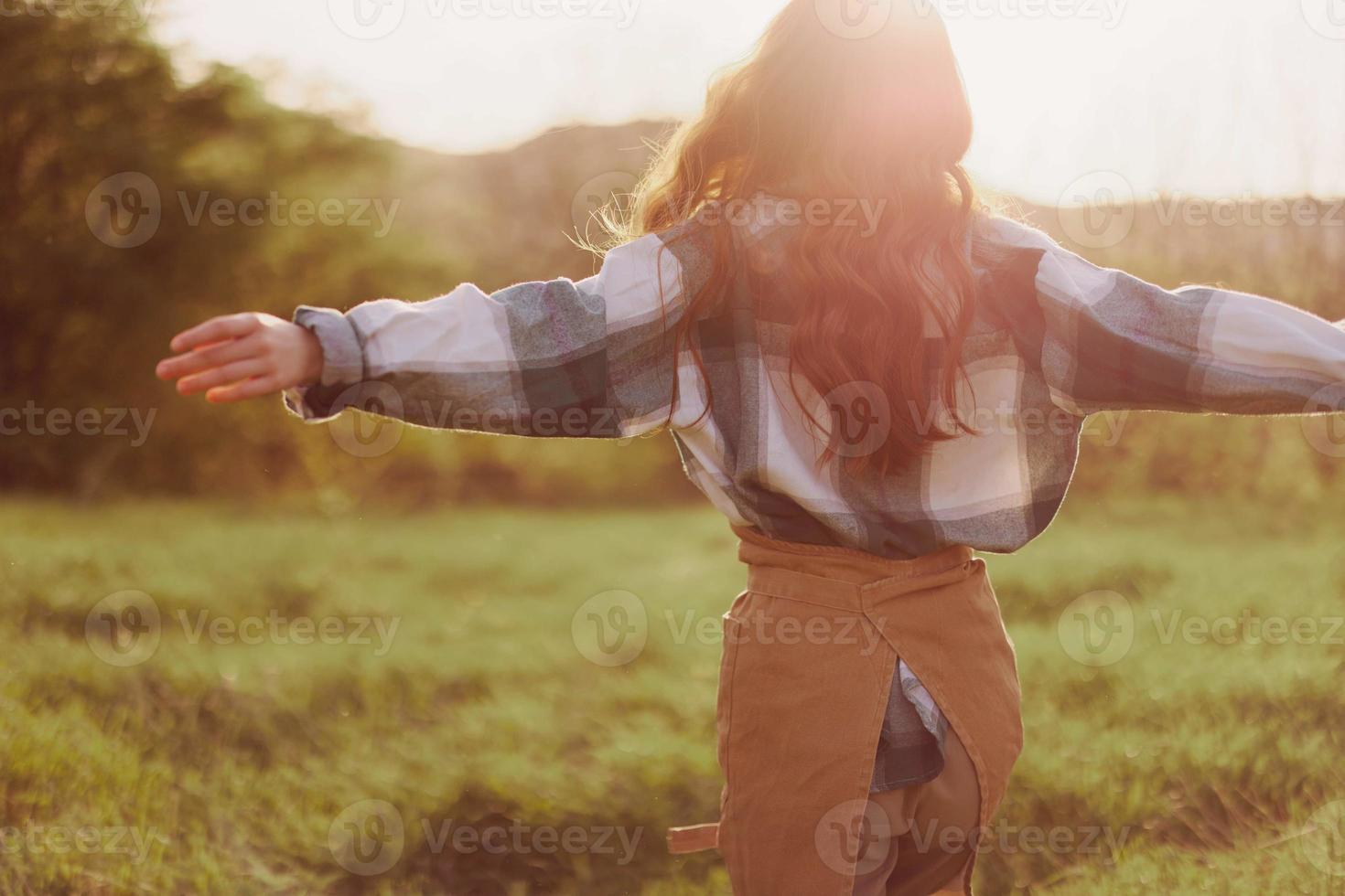une femme court à travers une champ avec sa retour à le caméra sur une été journée avec sa cheveux longue et en volant dans le le coucher du soleil. le concept de liberté et harmonie avec la nature photo