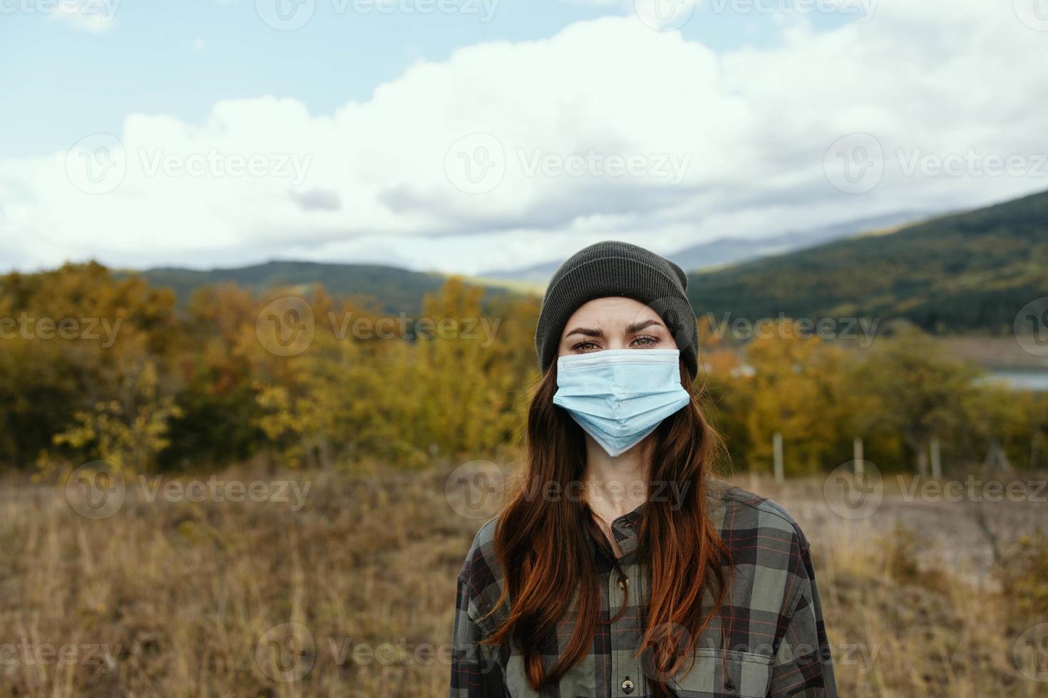 femme dans chaud casquette dans une médical masque dans le l'automne forêt dans le montagnes photo