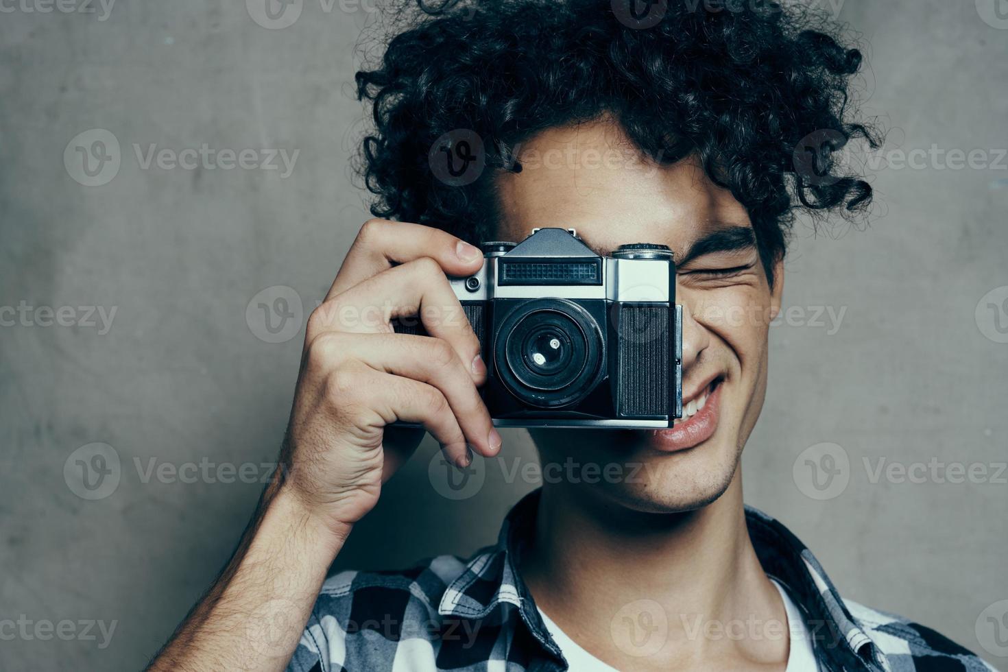 Beau gars avec une caméra près le sien visage et frisé cheveux plaid chemise loisir photographe photo