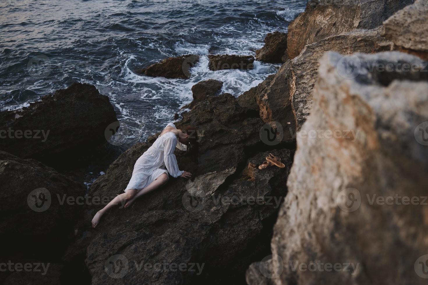 de haut en bas aérien vue de magnifique Jeune femme dans longue blanc robe mensonge sur rocheux côte avec des fissures sur rocheux surface photo