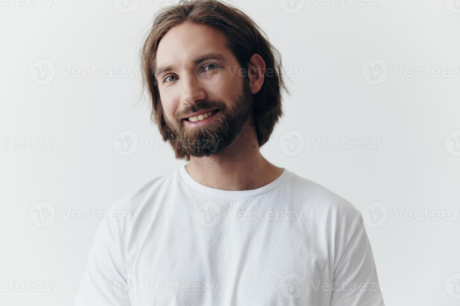 portrait de une de bonne humeur homme avec une noir épais barbe et longue cheveux avec une gentil sourire dans une blanc T-shirt sur une blanc isolé Contexte photo