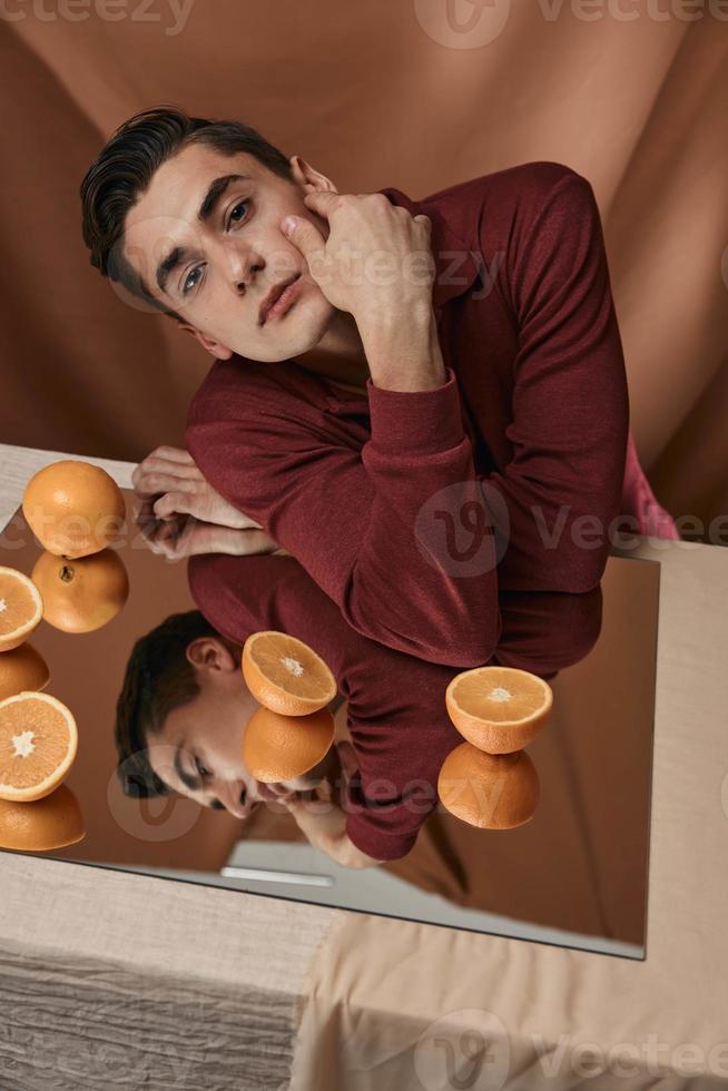 attrayant homme est assis à le table des oranges miroir fermer photo
