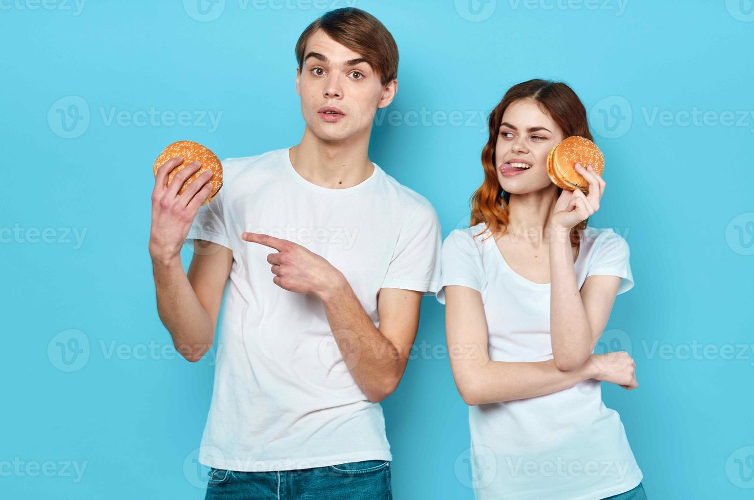 Jeune couple hamburgers dans mains casse-croûte mode de vie bleu Contexte photo