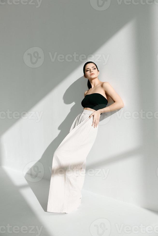 une à la mode femme dans une noir T-shirt et une blanc jupe est penché contre une mur à l'intérieur et une ombre est chute photo