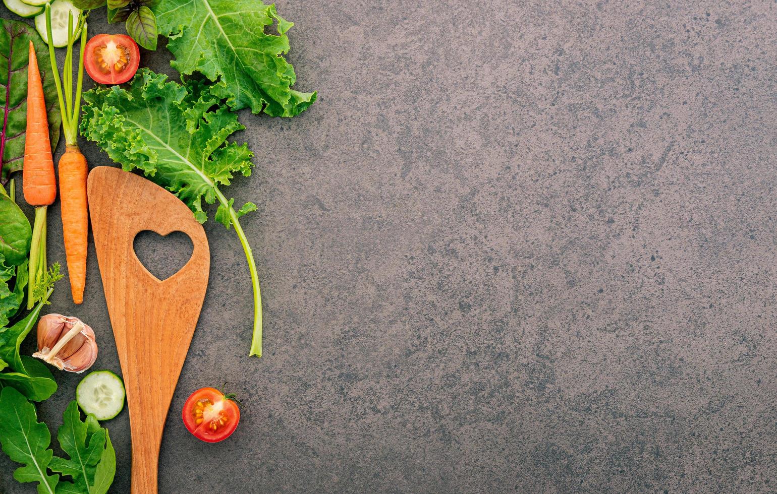 spatule en bois et légumes sur fond de pierre sombre. alimentation saine et concept de cuisine. photo