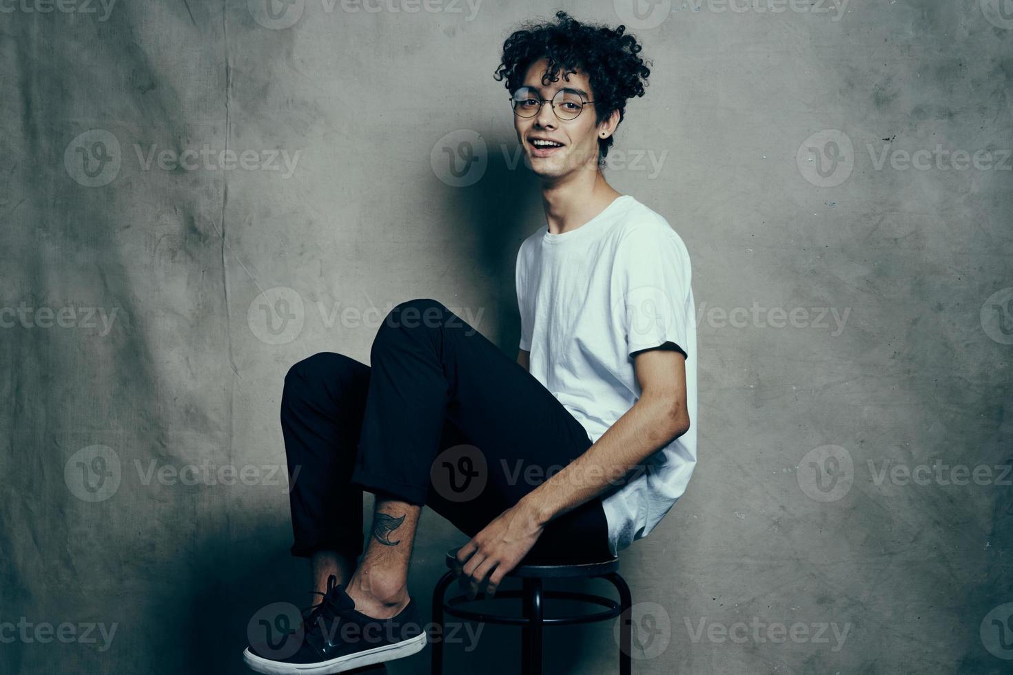 mignonne gars séance sur une chaise frisé cheveux sourire mode de vie photo