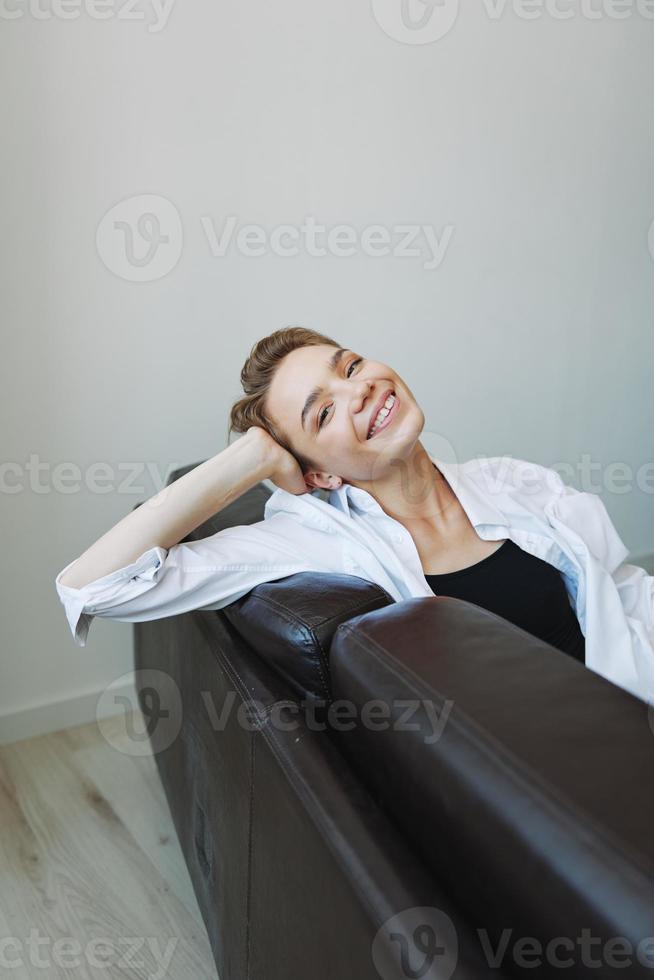 femmes mensonge à Accueil sur le canapé portrait avec une court la Coupe de cheveux dans une blanc chemise, sourire, la dépression dans adolescents, Accueil vacances photo