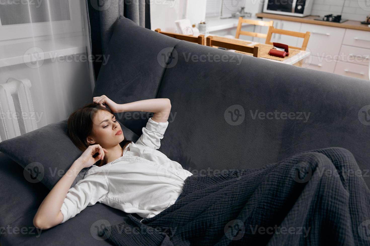 une femme dans une blanc T-shirt mensonges sur le canapé en dessous de une couverture et gestes avec sa mains photo