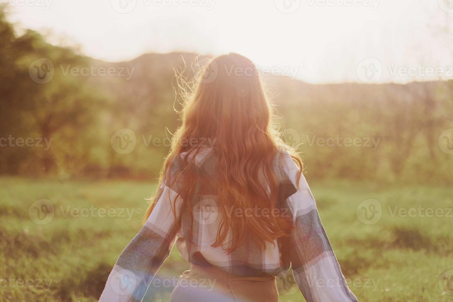 une femme court à travers une champ avec sa retour à le caméra sur une été journée avec sa cheveux longue et en volant dans le le coucher du soleil. le concept de liberté et harmonie avec la nature photo