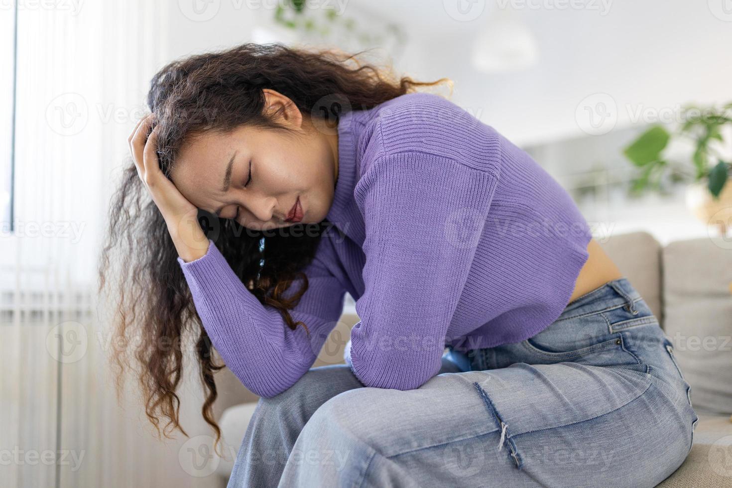 asiatique femme dans douloureux expression en portant mains contre ventre Souffrance menstruel période douleur, mensonge triste sur Accueil lit, ayant ventre crampe dans femelle santé concept photo