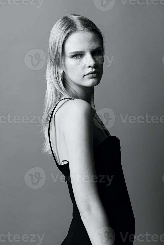 élégant noir et blanc portrait dans studio avec magnifique professionnel blond Jeune femelle femme dans peu noir robe regards à caméra posant isolé. cool offre pour mode marques photo