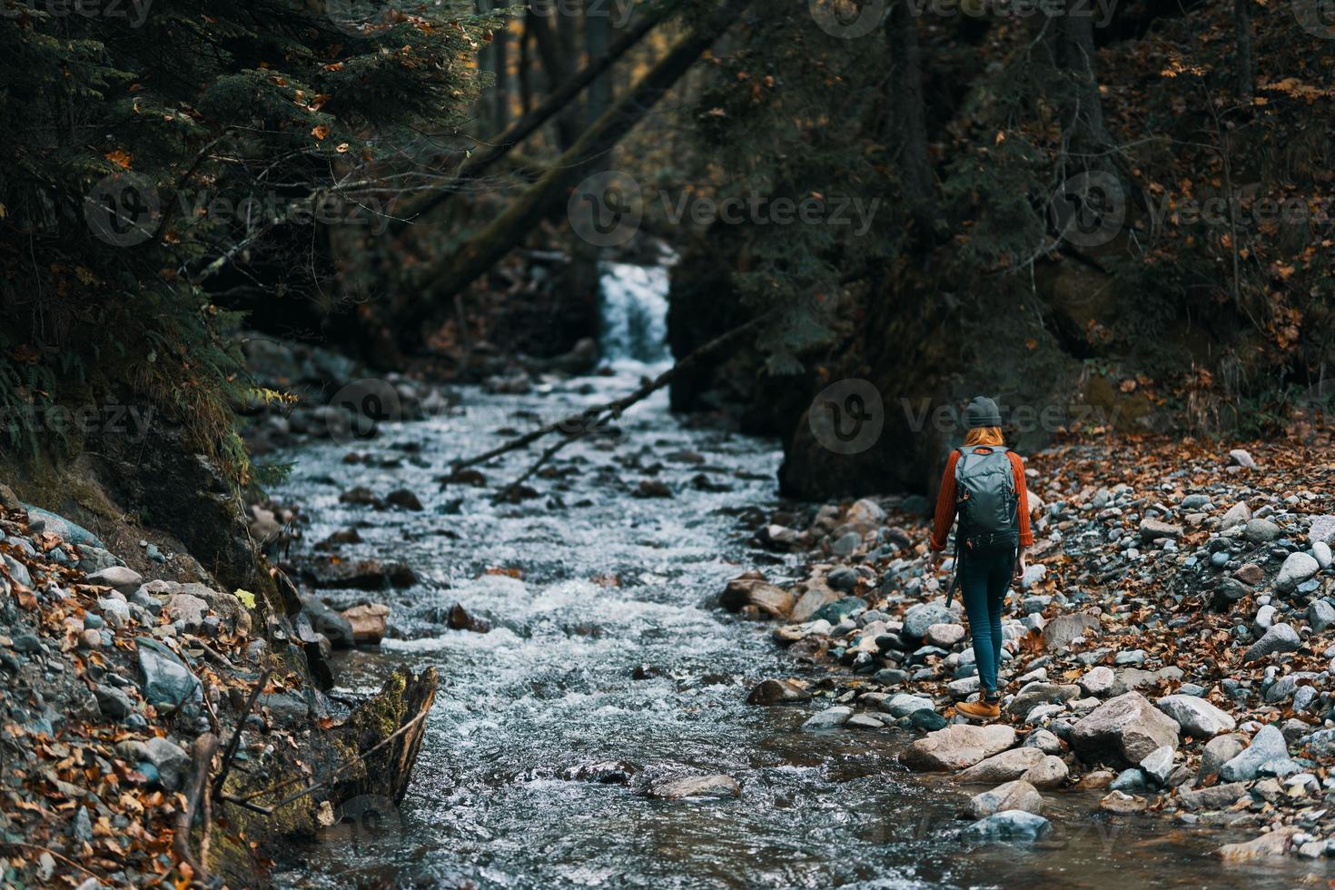 femme dans le montagnes près le rivière avec une sac à dos sur sa retour et une forêt dans le Contexte photo