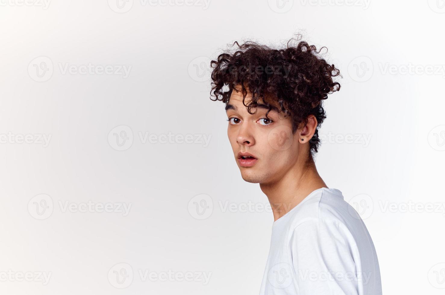 énergique gars avec frisé cheveux dans une blanc T-shirt sur une lumière Contexte photo