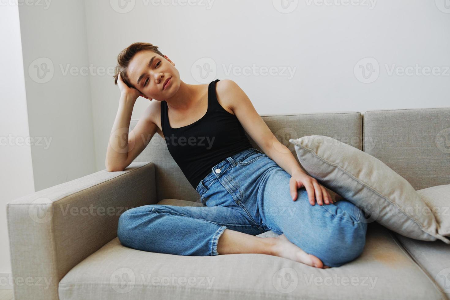 Jeune femme avec court la Coupe de cheveux cheveux ayant amusement à Accueil sur le canapé sourire et bonheur, vacances à maison, Naturel posant sans pour autant filtres, gratuit copie espace photo