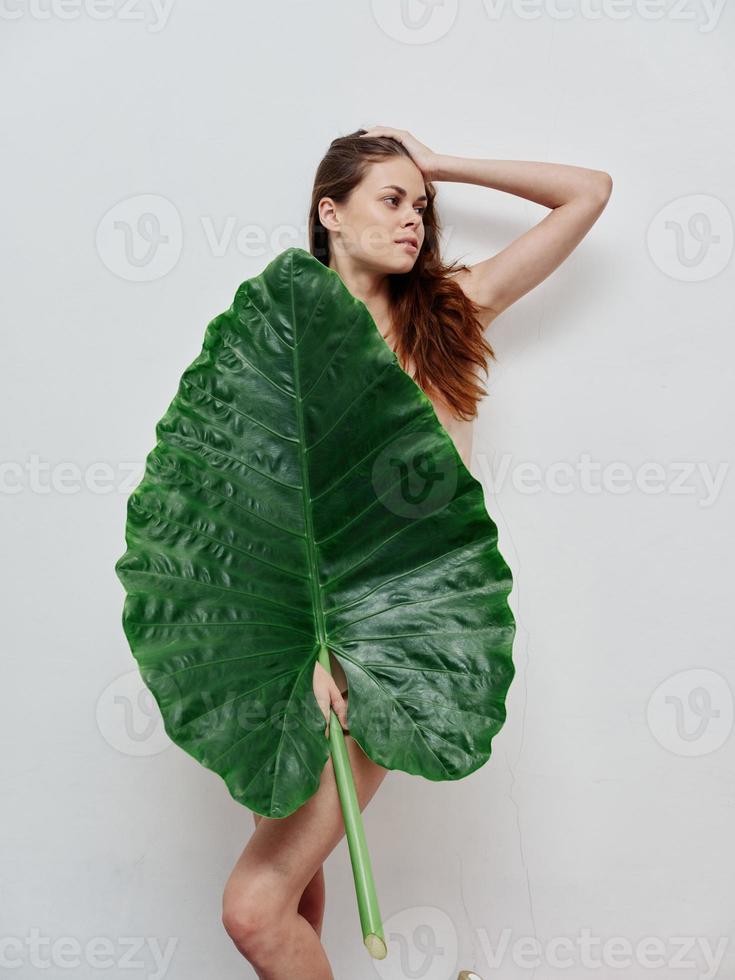 femme avec une nu corps une grand vert feuille dans sa mains lumière Contexte photo