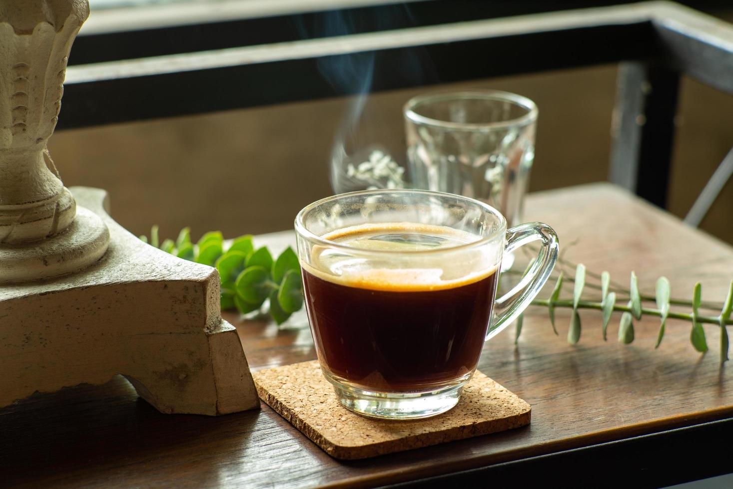 Verre gros plan de café noir chaud avec de la fumée sur la table en bois photo