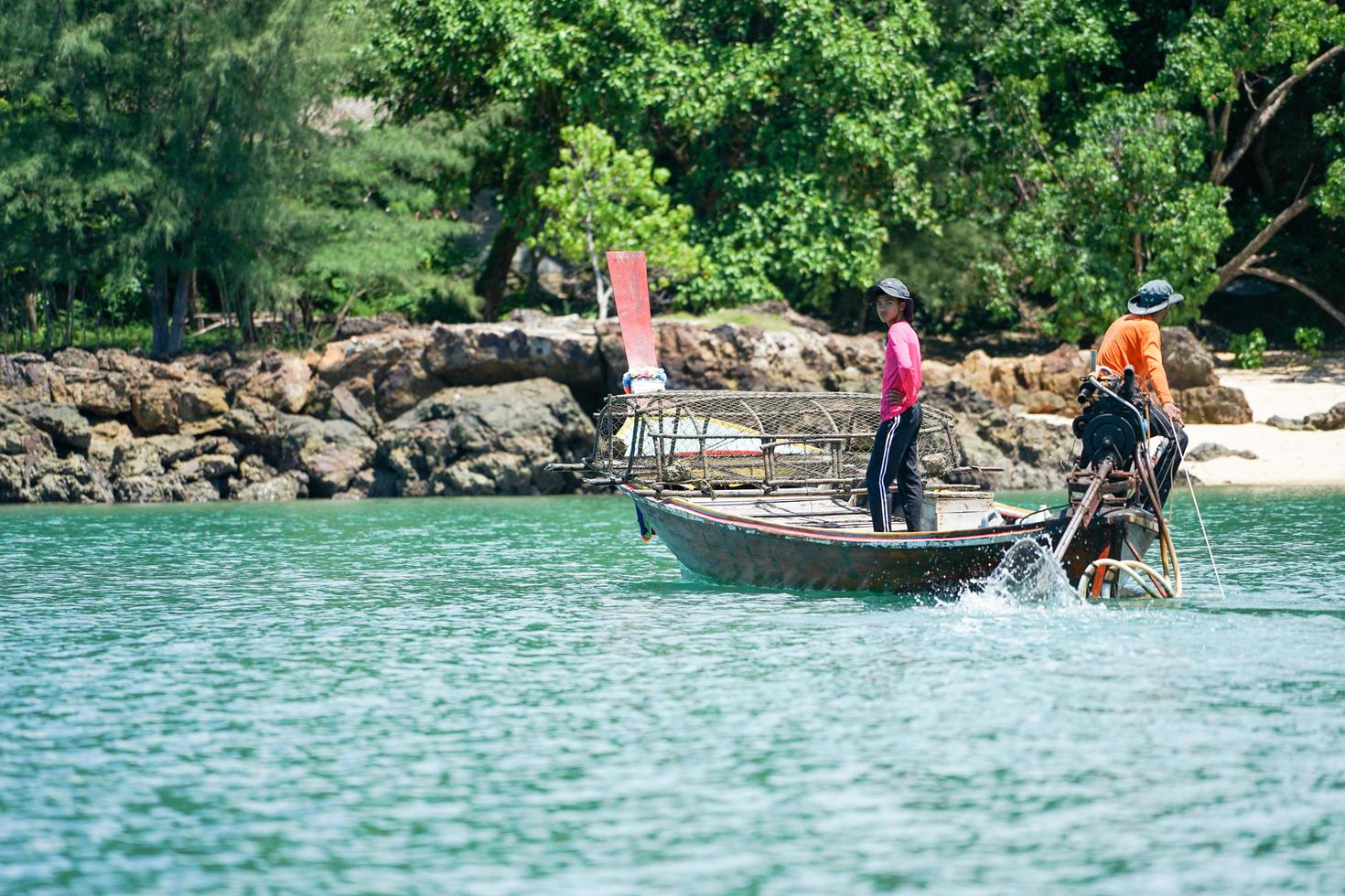 Ko Lanta, Krabi, Thaïlande 2019 - Les pêcheurs conduisent le bateau traditionnel à longue queue et trouvent du poisson par des outils en journée ensoleillée avec une île défocalisée en arrière-plan photo