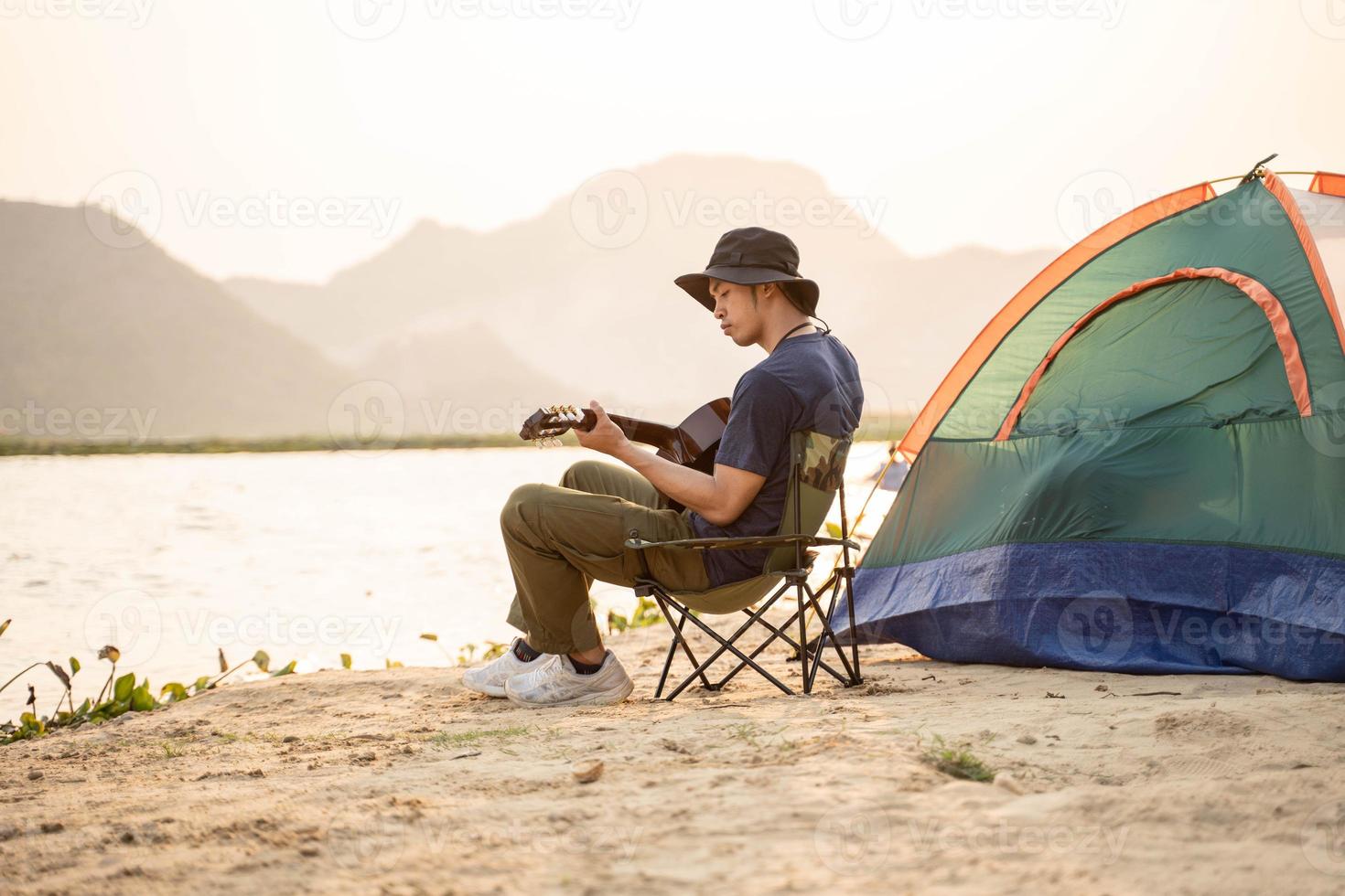 homme camping touristique avec acoustique guitare séance sur le sable plage en chantant et en jouant guitare près touristique tente photo