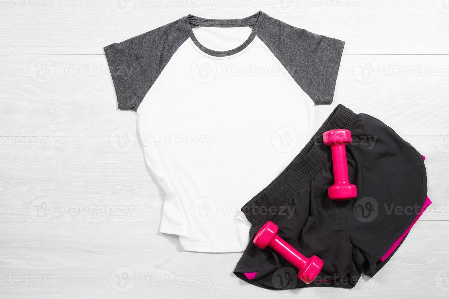 blanc femelle sport t chemise moquer en haut plat allonger sur en bois Contexte. été accessoires. sportif pantalon, rose femelle haltères. Haut de face vue T-shirt. maquette T-shirt. modèle Vide copie espace photo