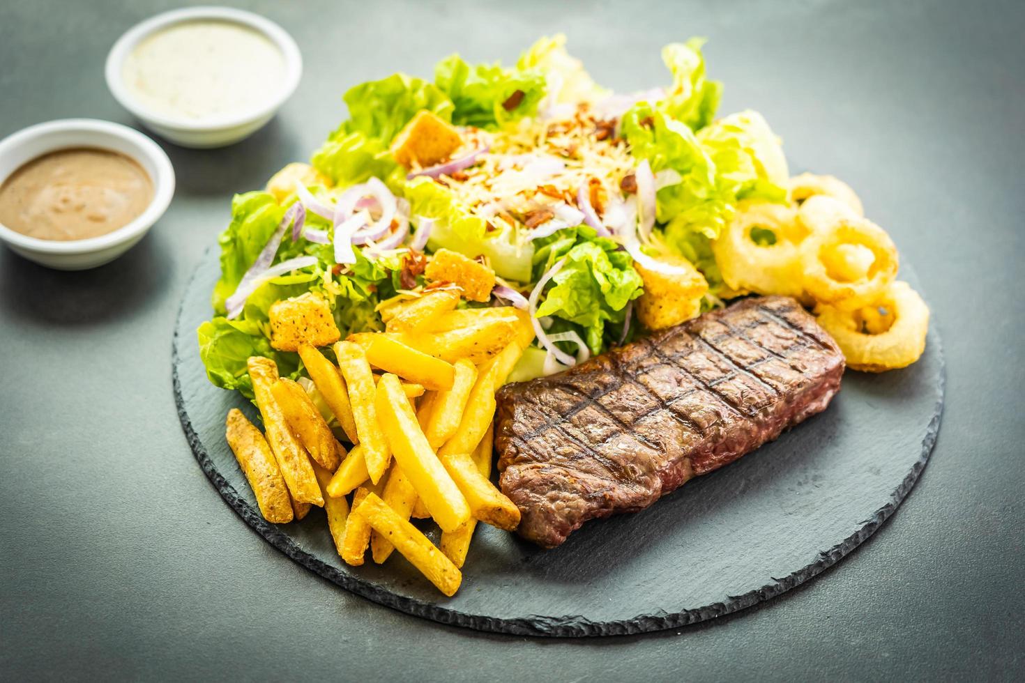 Steak de viande de bœuf grillé avec frites rondelle d'oignon avec sauce et légumes frais photo