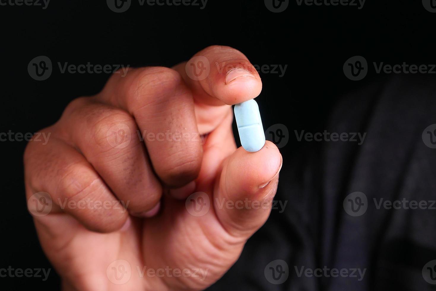 main tenant la pilule bleue sur fond noir photo