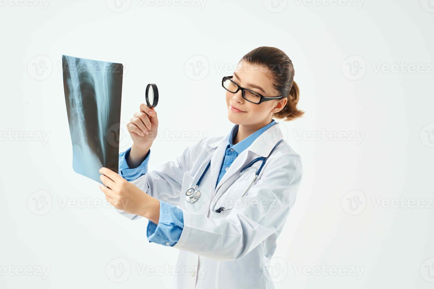 une infirmière dans une blanc manteau regards à un radiographie par une grossissant verre photo