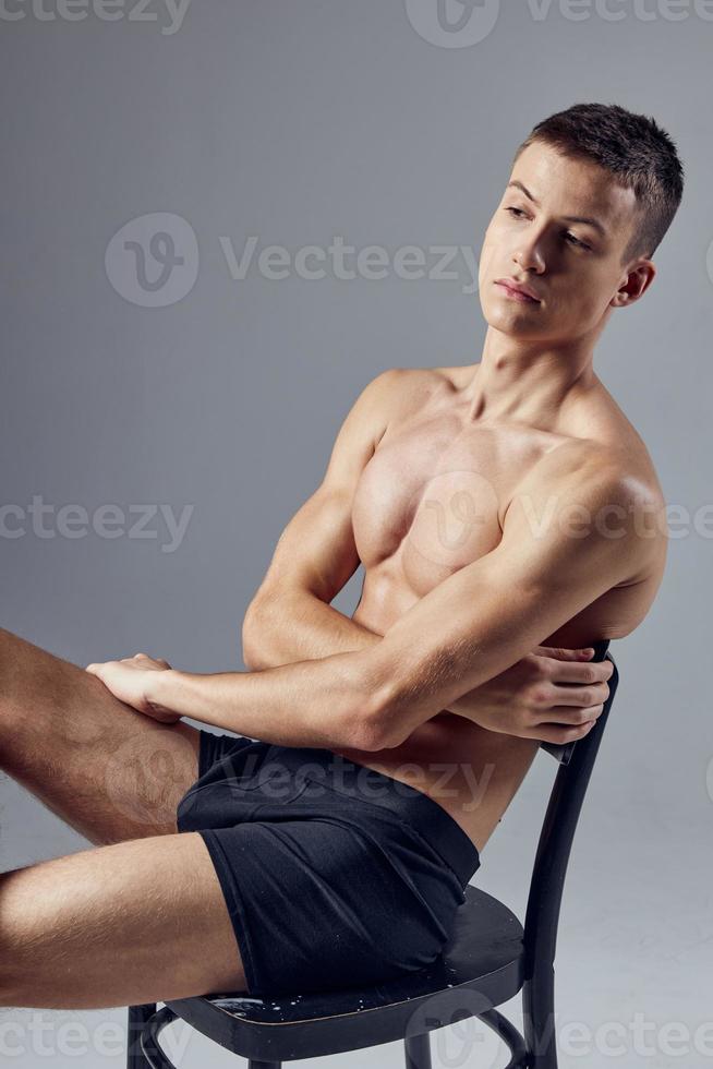 portrait de une sportif homme avec une nu corps séance sur une chaise dans noir culotte photo